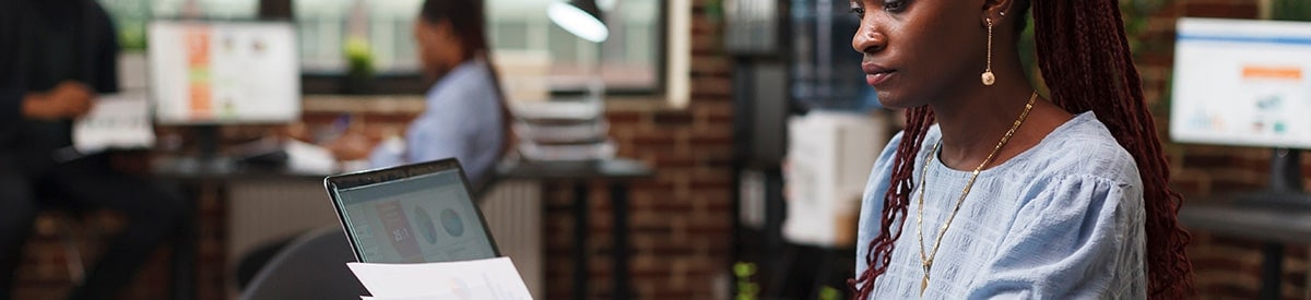 Eine Frau sitzt an einem Schreibtisch in einem Büro und prüft Papiere