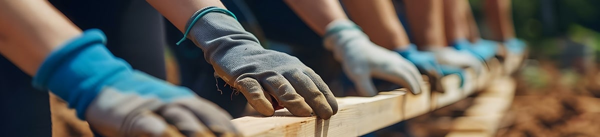 Menschen bei einem Projekt im Freien, die Handschuhe tragen und mit Holz arbeiten